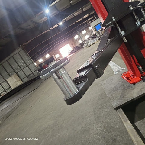 2-post vehicle lift in red installed in garage
Close-up of lifting arms and safety lock mechanism
Base of hoist with truck tires for scale
Top bar and hydraulic system β JH5000F model