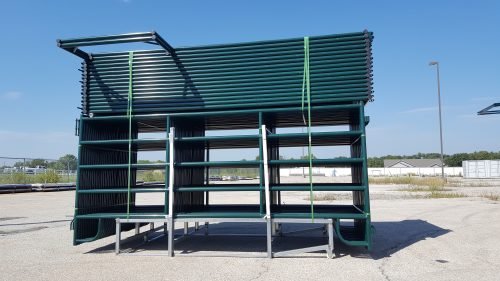 Green steel livestock corral panels with built-in entrance gate stacked on gravel lot
