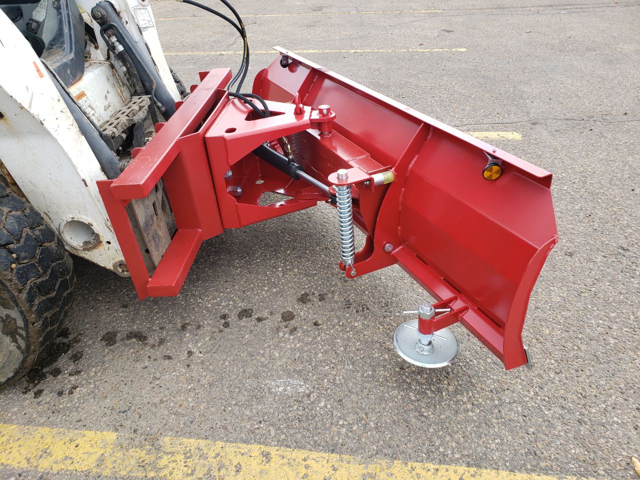 Skid steer clearing snow using Bendall hydraulic snow plow

Bendall 96” red snow plow angled to the side

Close-up of adjustable skid shoes and hydraulic fittings

Rear view of snow blade attached to skid steer

Bolt-on reversible cutting edge on Bendall plow