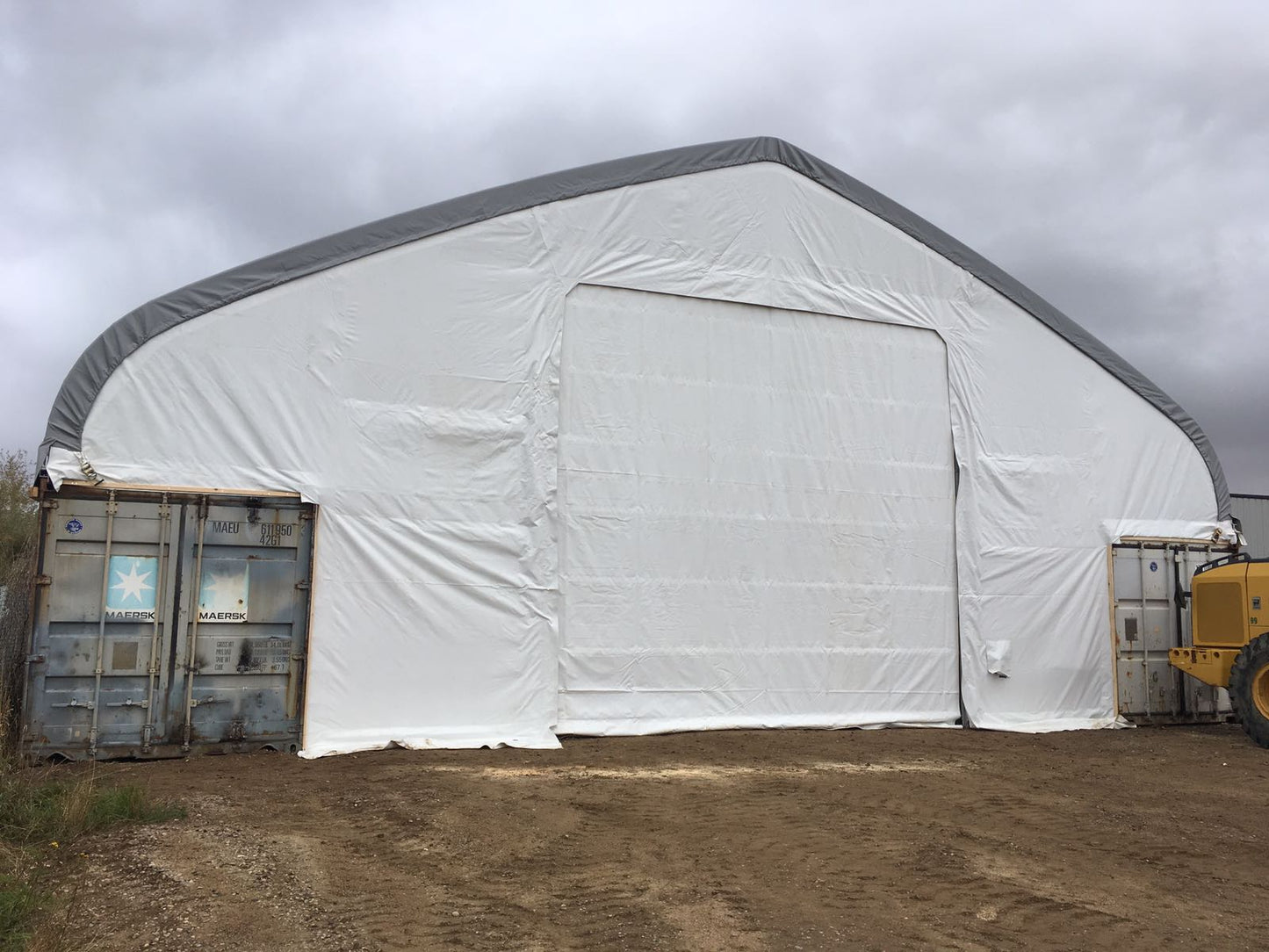 50x80 ft all-white PVC double truss fabric shelter installed over shipping containers – heavy-duty industrial storage building