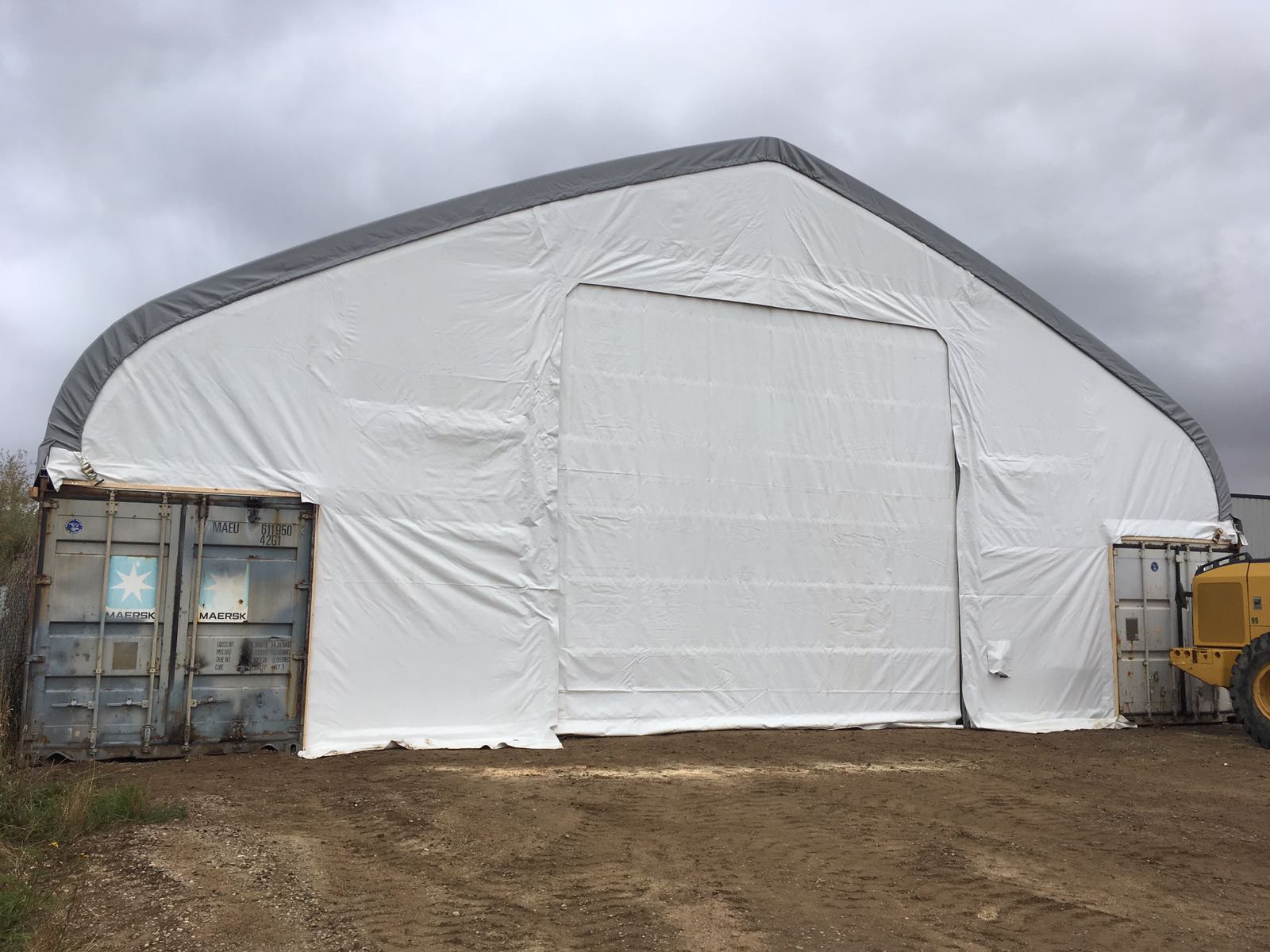 50x80 ft all-white PVC double truss fabric shelter installed over shipping containers – heavy-duty industrial storage building