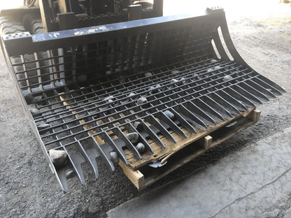 96" skid steer rock bucket with ½" spacing

Heavy-duty skeleton rock bucket on gravel

Close-up of angled bar structure

72" deluxe rock grapple for small rocks and debris

Skid steer lifting rock bucket attachment

