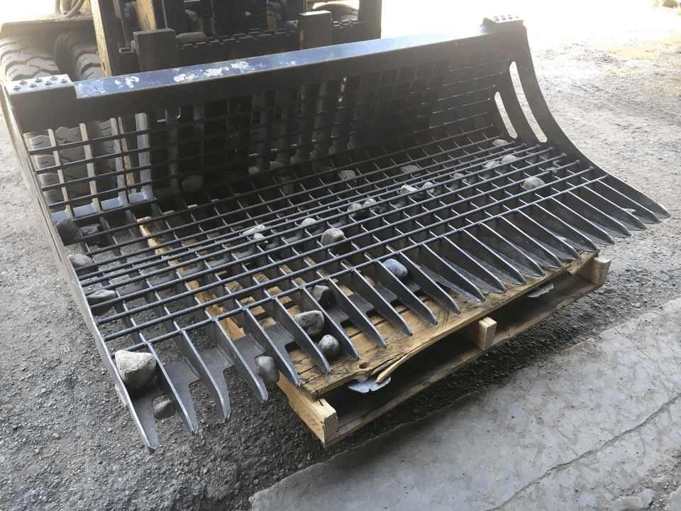 96" skid steer rock bucket with ½" spacing

Heavy-duty skeleton rock bucket on gravel

Close-up of angled bar structure

72" deluxe rock grapple for small rocks and debris

Skid steer lifting rock bucket attachment

