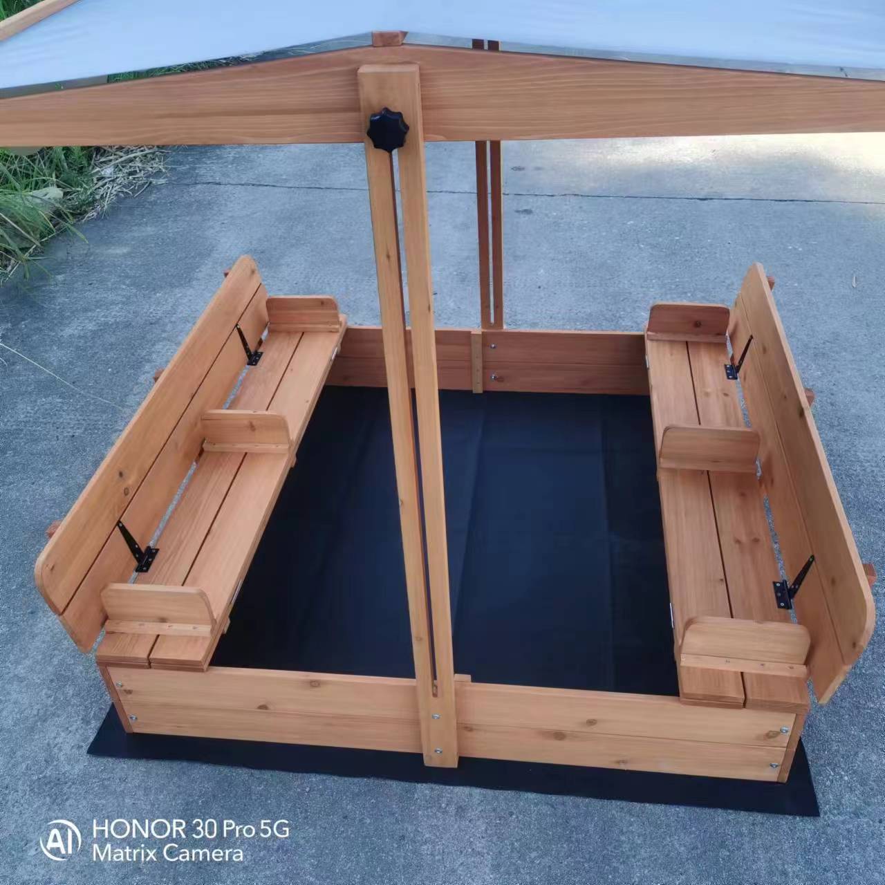 Wooden sandbox with canopy fully extended and benches visible

Close-up of sandbox lid cover in closed position

Children playing inside wooden sandbox with canopy

Side angle showing bench detail and canopy fabric

Folded sandbox closed with protective cover on top