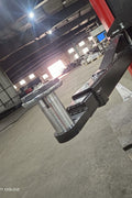 2-post vehicle lift in red installed in garage

Close-up of lifting arms and safety lock mechanism

Base of hoist with truck tires for scale

Top bar and hydraulic system – JH5000F model