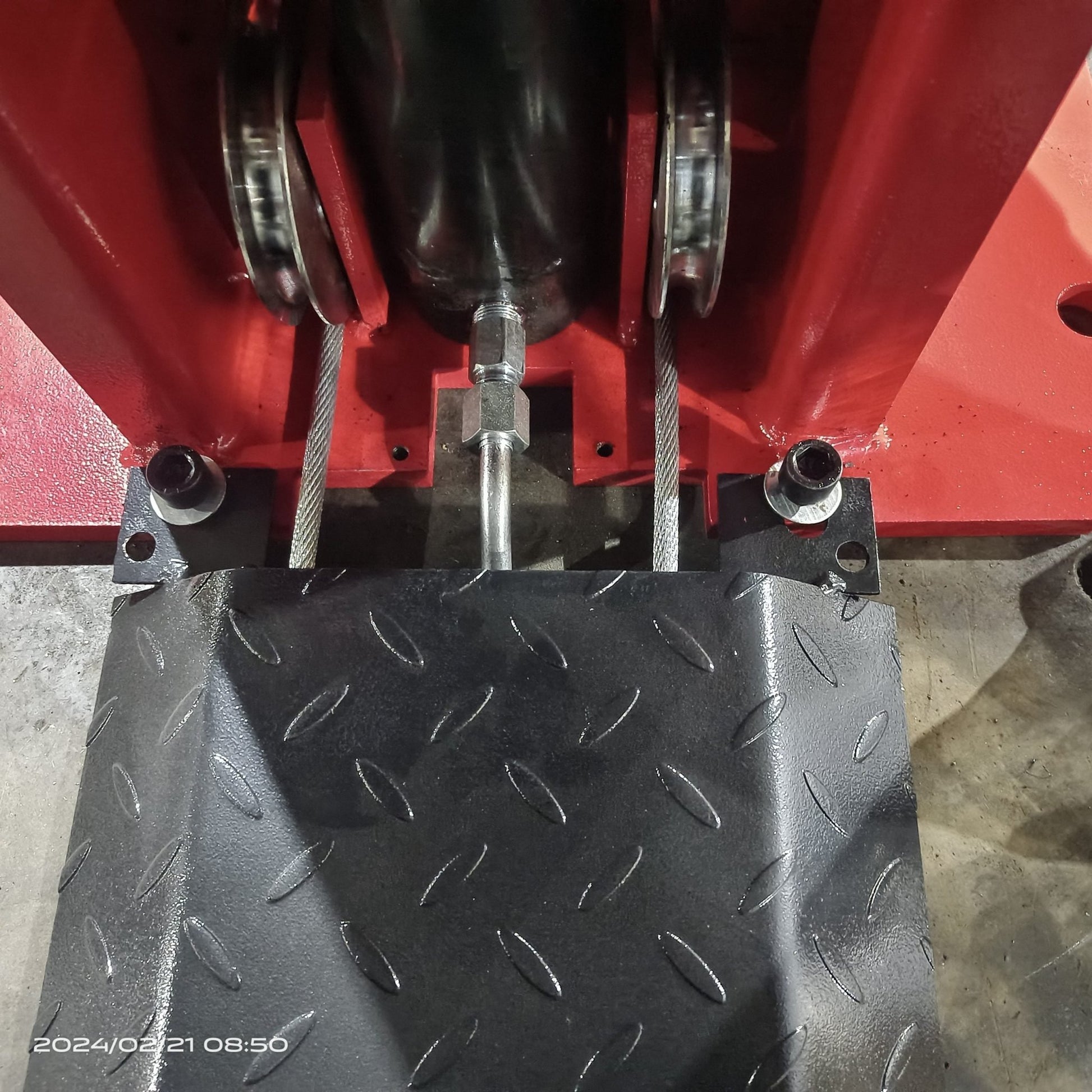 2-post vehicle lift in red installed in garage

Close-up of lifting arms and safety lock mechanism

Base of hoist with truck tires for scale

Top bar and hydraulic system – JH5000F model