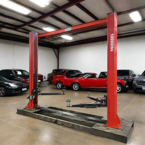 2-post vehicle lift in red installed in garage

Close-up of lifting arms and safety lock mechanism

Base of hoist with truck tires for scale

Top bar and hydraulic system – JH5000F model