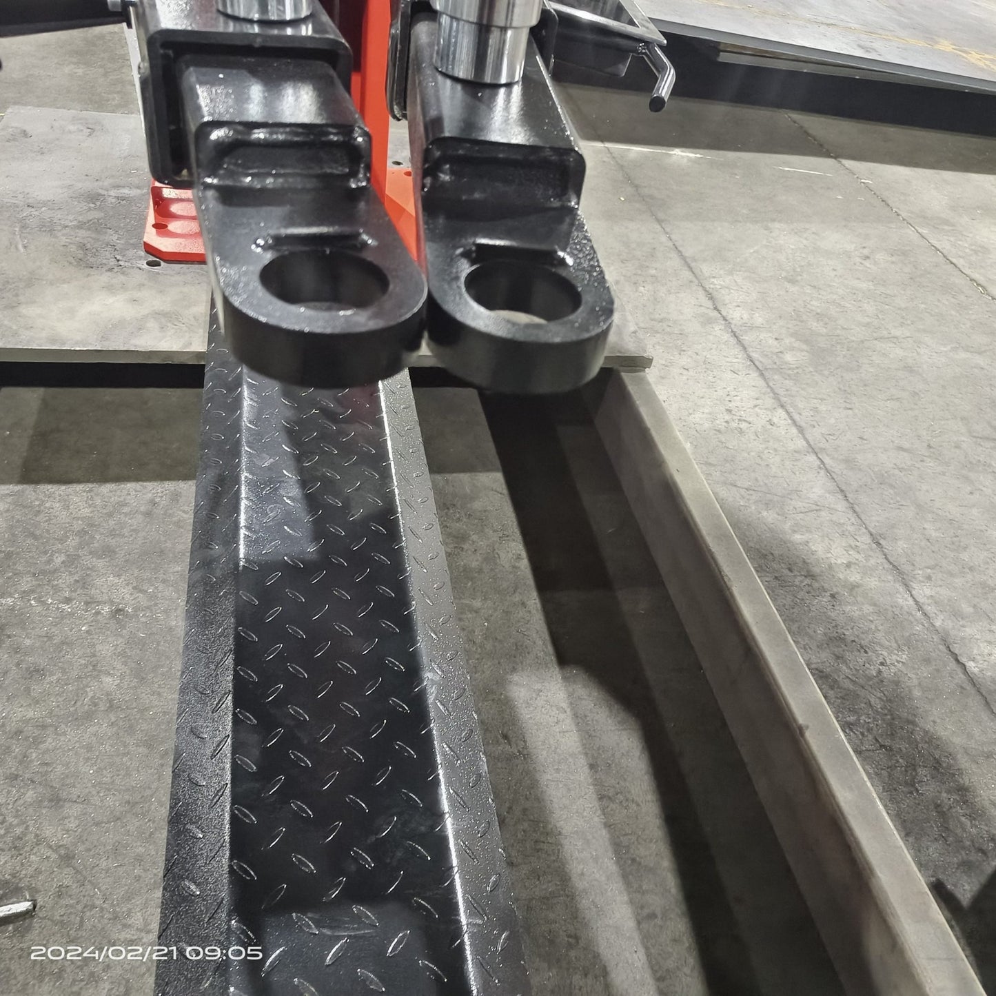 2-post vehicle lift in red installed in garage

Close-up of lifting arms and safety lock mechanism

Base of hoist with truck tires for scale

Top bar and hydraulic system – JH5000F model