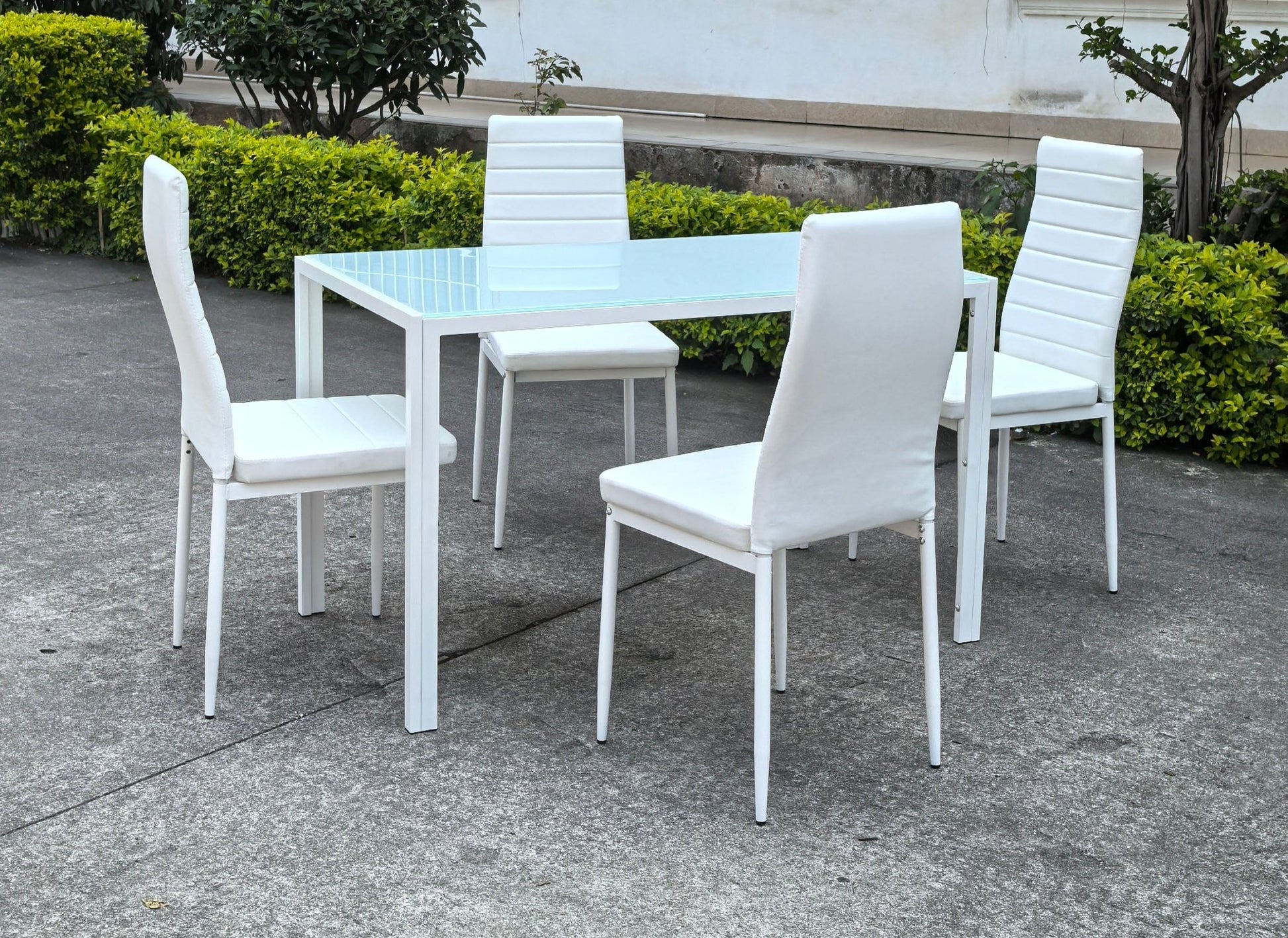 White glass dining table set with 4 chairs in the bright kitchen
Close-up of white glass table and upholstered chair
Side angle of a full 5-piece dining set
White dining chairs around a modern glass table
Dining set outdoors showing full product design
