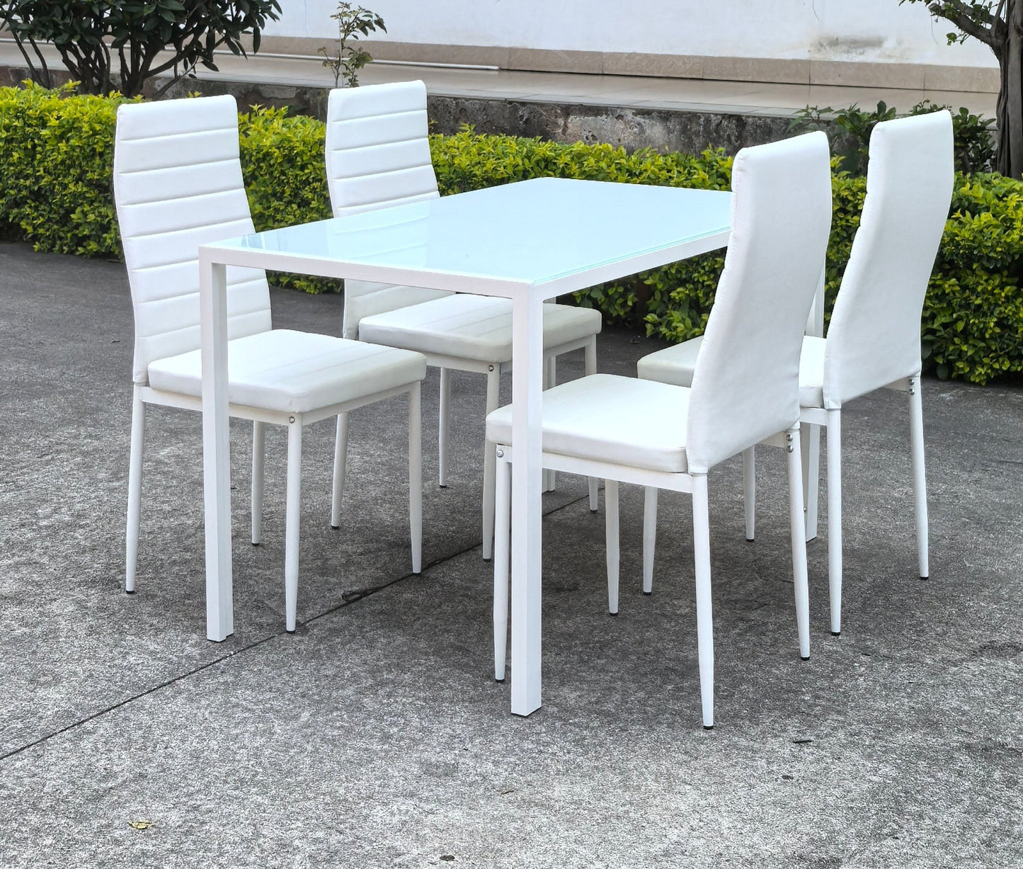 White glass dining table set with 4 chairs in the bright kitchen
Close-up of white glass table and upholstered chair
Side angle of a full 5-piece dining set
White dining chairs around a modern glass table
Dining set outdoors showing full product design