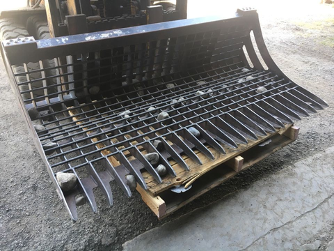 96" skid steer rock bucket with ½" spacing

Heavy-duty skeleton rock bucket on gravel

Close-up of angled bar structure

72" deluxe rock grapple for small rocks and debris

Skid steer lifting rock bucket attachment

